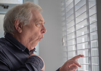 Senior man with funny facial expression spying through window blinds 