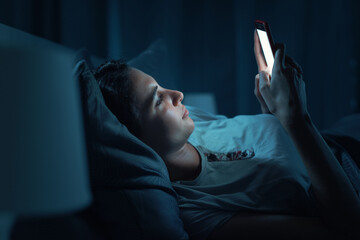 Young woman lying in bed and using her smartphone