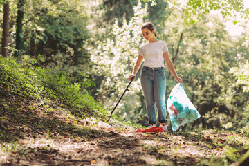 Fototapeta Girl cleaning up the forest and collecting trash obraz