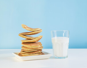 Levitating stack of pancakes with honey and glass of milk on a blue background.  Levitation, gravity. Homemade breakfast.Maslenitsa. Shrovetide. Shrove Tuesday. Pancake Day. Happy holiday, Greeting. D