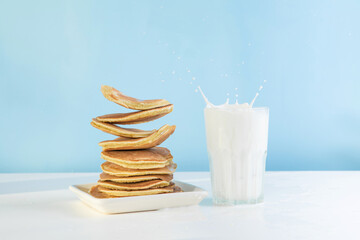 Levitating stack of pancakes with honey and glass of milk. Splash of milk from the glass on a blue background.  Levitation, gravity. Homemade breakfast.Maslenitsa. Shrovetide. Shrove Tuesday. Pancake 