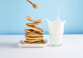Levitating stack of pancakes with honey and glass of milk. Splash of milk from the glass on a blue background.  Levitation, gravity. Homemade breakfast.Maslenitsa. Shrovetide. Shrove Tuesday. Pancake 