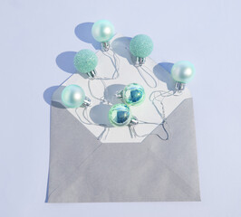 Shiny, pastel green Christmas baubles (balls) getting out of a gray envelope on a blue background. Minimalist concept. Events and anniversaries. Newborn baby card template. Copy paste. Flat lay.