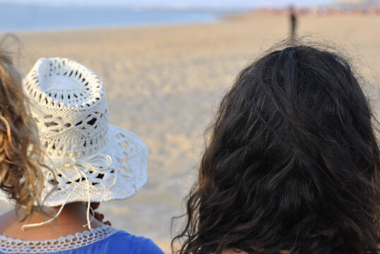 Close-up of two women on their backs looking at the beach, one of them wearing a hat.