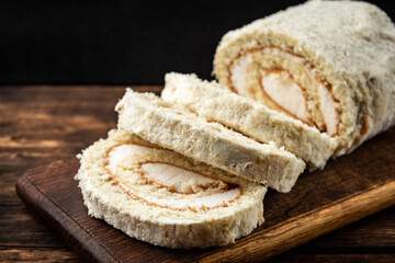 Coconut sponge cake roll biscuit on dark wooden background.