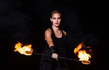 Sexy woman performer twirl burning baton during fire performance in dark night outdoors, partyin