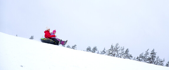The family goes downhill on an inflatable ring, winter entertainment. A young woman and a child ride down a snowy mountain.