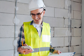Happy construction engineer looking at his phone, scrolling