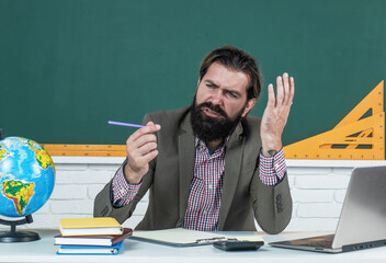 out of ink. confused man with beard work on computer. studying online. informal education. male student sit in school classroom on lesson with blackboard. pass the exam. learning the subject