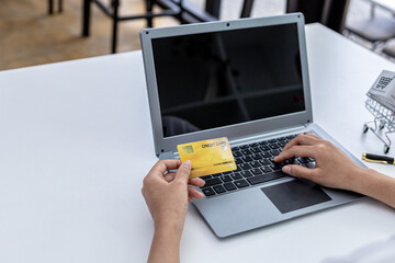 Woman holding credit card and typing on a laptop keyboard, she is filling out credit card information to pay for an order on an internet shopping site. Online shopping and credit card payment concept