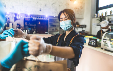Fototapeta na wymiar Young chinese owner of a restaurant wearing protective mask and gloves while is delivering food to her clients safely.