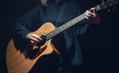 A young woman with an acoustic guitar in the dark under a ray of light.