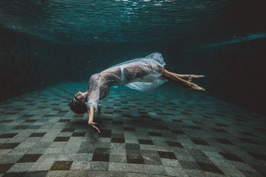 Young dark hair woman in vintage white dress swim underwater. Floating in the swimming pool. Fantastic and Fairy dreamy fashion. Turquoise water.