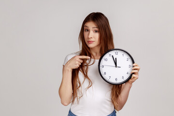 Portrait of beautiful punctual woman pointing finger at white display of big wall clock seriously...