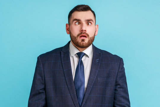 Funny amused man with beard wearing official style suit crossing his eyes looking crazy and stupid, fooling around, having fun, vision problems. Indoor studio shot isolated on blue background.