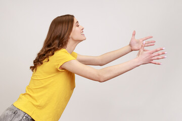 Side view of kind young female with brown hair outstretching hands as if giving for free, offering...