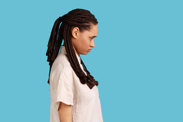 Side view of offended woman with dreadlocks looking with sulking frowning face, waits for explanations or apology, being irritated with unfair thing. Indoor studio shot isolated on blue background.