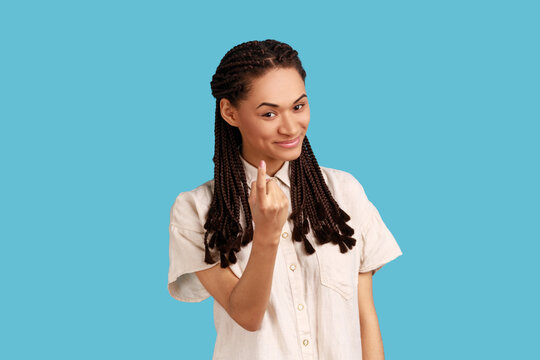 Attractive young woman with black dreadlocks looks with appeal at camera, says come here, gestures with index finger, has mysterious expression. Indoor studio shot isolated on blue background.