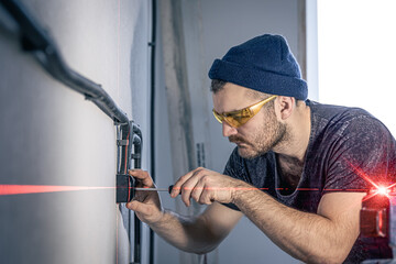An electrician is mounting electric sockets on the white wall indoors.