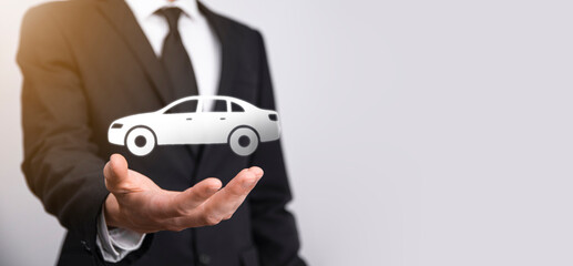 Male hand holding car auto icon on grey background. Wide banner composition.Car automobile insurance and collision damage waiver concepts