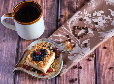Homemade baked cake Napoleon, Millefeuille. Delicate custard cake garnished with berries. Against the background of a wooden table with a beautiful napkin and whole coffee beans