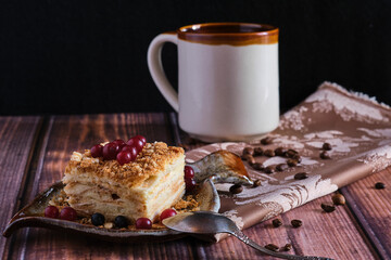 Homemade baked cake Napoleon, Millefeuille. Delicate custard cake garnished with berries. Against the background of a wooden table with a beautiful napkin and whole coffee beans