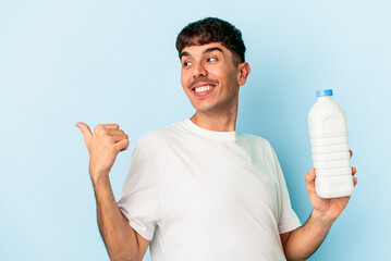 Young mixed race man holding a bottle of milk isolated on blue background points with thumb finger away, laughing and carefree.