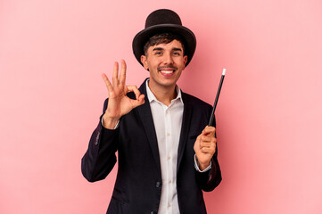 Young caucasian wizard man holding a wand isolated on pink background cheerful and confident showing ok gesture.