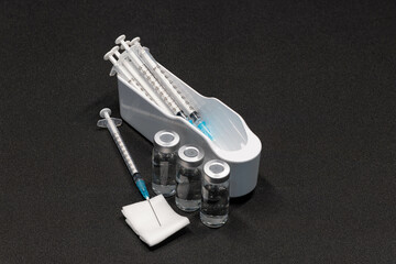 Medical Equipment that includes Syringes with Hypodermic Needles with Safety Caps and vials Containing a clear Liquid.