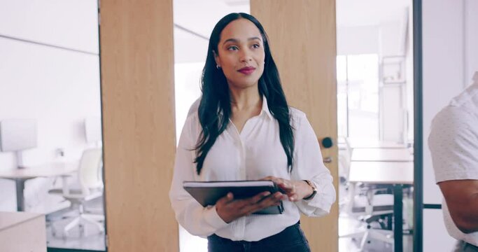 Young business woman walking through a modern office. Confident businesswoman using a digital tablet and greeting her colleagues while checking her digital notes. Young female boss arriving at work.