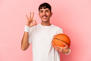 Young mixed race man playing basketball isolated on pink background cheerful and confident showing ok gesture. © Asier