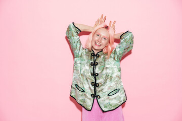 Young white woman in chinese jacket smiling while making horn gesture