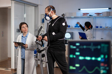 Sportman with medical electrodes on it running on fitness trainer working at body endurance during medical workout in modern laboratory while doctor monitoring EGK data. Heart rate pulse on monitor