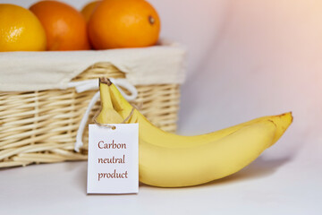 Carbon neutral product label on bananas. Carbon labeling. Basket of oranges on background. Net zero...
