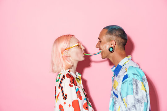 Young couple in multicolored shirts laughing while eating chewing candy
