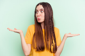 Young caucasian woman isolated on green background confused and doubtful shrugging shoulders to...
