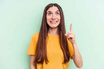 Young caucasian woman isolated on green background indicates with both fore fingers up showing a...