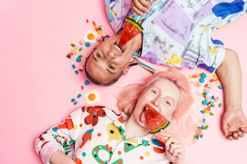 Young couple licking lollipops while lying with candies on floor