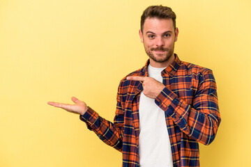 Young caucasian man isolated on yellow background excited holding a copy space on palm.