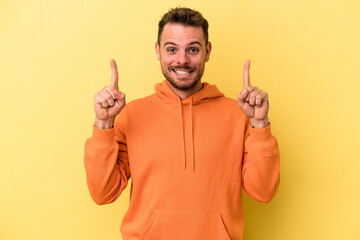Young caucasian man isolated on yellow background indicates with both fore fingers up showing a...