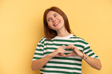 Young English woman isolated on yellow background smiling and showing a heart shape with hands.