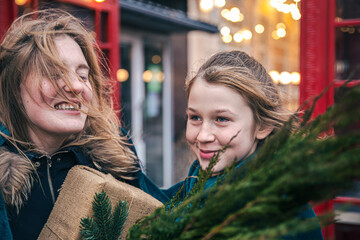 A little girl and young woman with thuja branches and a gift under a plaid.