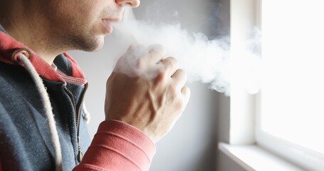 Close-up of a man smokes an electronic cigarette. Smoke comes from the nose and mouth.