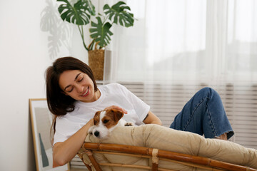 Portrait of young beautiful woman lying on a papasan chair with her adorable wire haired Jack Russel terrier puppy. Loving girl with rough coated pup on saucer chair. Background, close up, copy space.