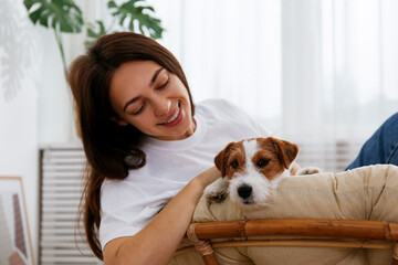 Portrait of young beautiful woman on a papasan chair with her adorable wire haired Jack Russel terrier puppy. Loving girl with rough coated pup having fun. Background, close up, copy space.