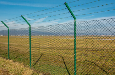 Green steel wire mesh fence around the airport area. Restricted area protection.