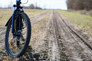 Obraz premium front wheel of a mountain bike. Mountain bike. stands on a field road. concept of cycling, repair or breakage, sports, outdoor activities. bike on trail, front wheel in focus. space for text