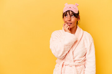 Young Argentinian woman wearing a pajama isolated on yellow background relaxed thinking about...