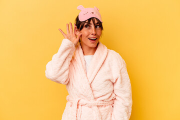 Young Argentinian woman wearing a pajama isolated on yellow background trying to listening a gossip.