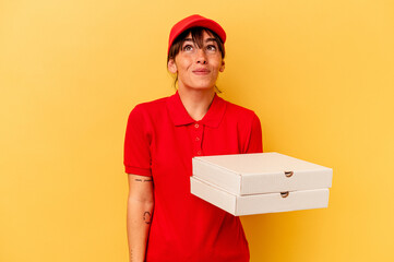 Young delivery woman holding pizzas isolated on yellow background dreaming of achieving goals and...
